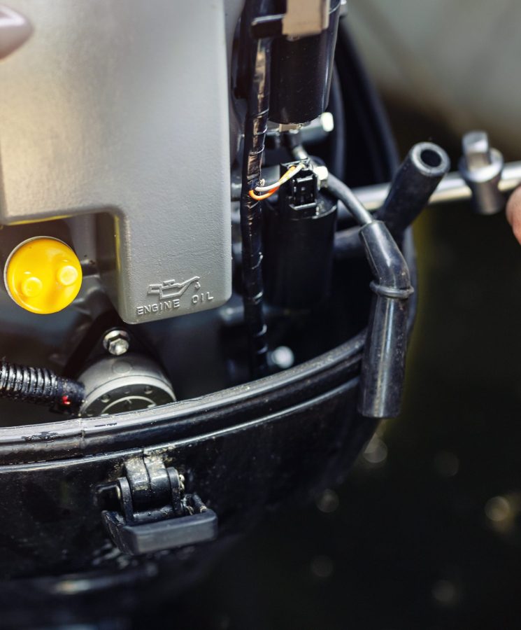 mechanic repairing inflatable motorboat engine at boat garage. Ship engine seasonal service and maintenance. Vessel motor with open cover.